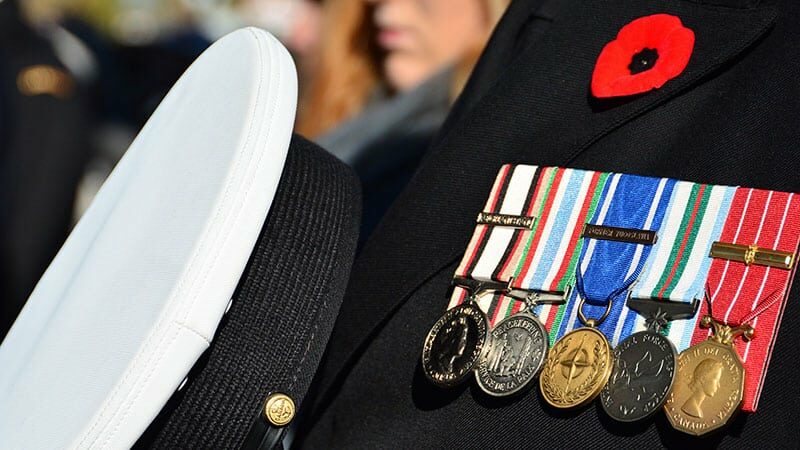 close up of formal military uniform with ribbon, hat over heart, and a poppy pinned to label