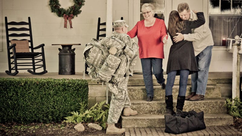 Soldier and his spouse are greeted by family with hugs at Christmas