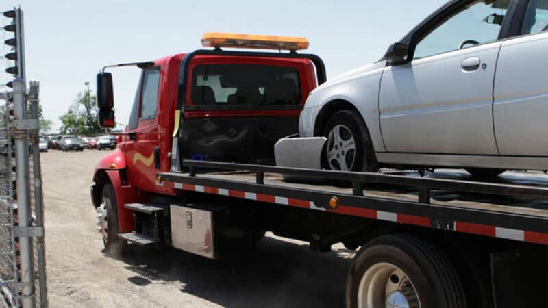 A flatbed truck tows away an old car